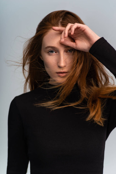 beautiful ginger woman in dark sweater looking at camera and posing on grey studio background - Zdjęcie, obraz