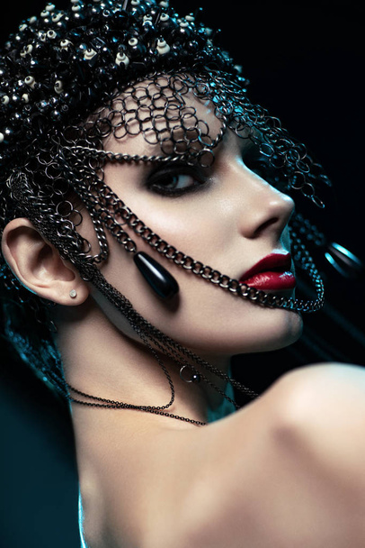 portrait of attractive brunette woman in designer headdress with chains posing on dark studio background - Photo, image