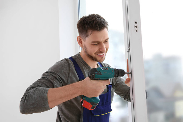 Construction worker using drill while installing window indoors - Φωτογραφία, εικόνα