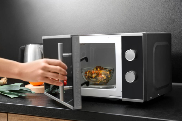 Young woman using microwave oven on table in kitchen - Foto, imagen