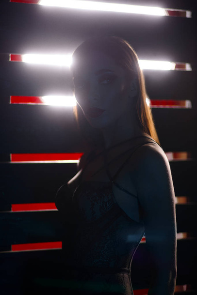 beautiful brunette woman in black lingerie posing near in dark studio with red stripes background - Foto, Imagem