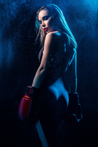 back view of beautiful woman with bright makeup wearing dress and boxing gloves posing on dark background  - Photo, Image
