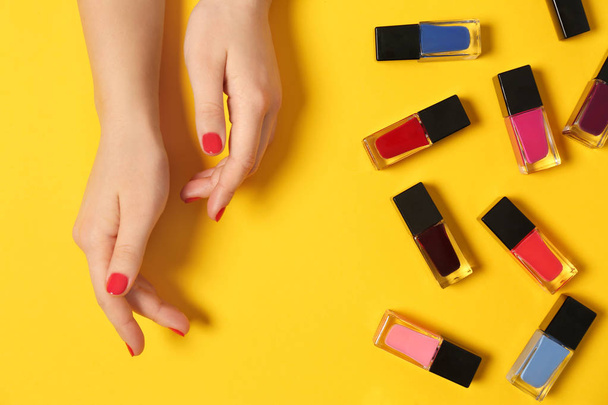 Woman with red manicure and nail polish bottles on color background, top view - Φωτογραφία, εικόνα