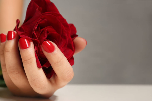 Woman with red manicure holding rose on blurred background, closeup. Nail polish trends - Photo, image
