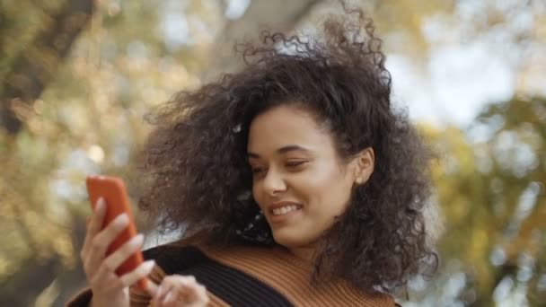 Beautiful young girl with dark curly hair using her phone in a city park.  - Кадри, відео
