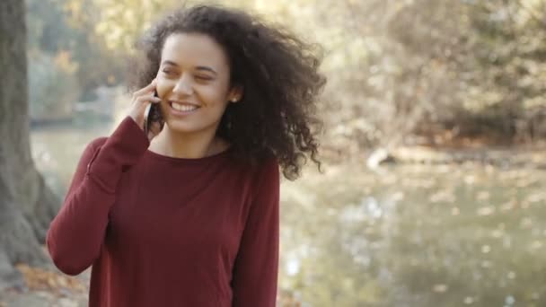 Beautiful young girl with dark curly hair using her cell phone, outdoor. - Filmmaterial, Video