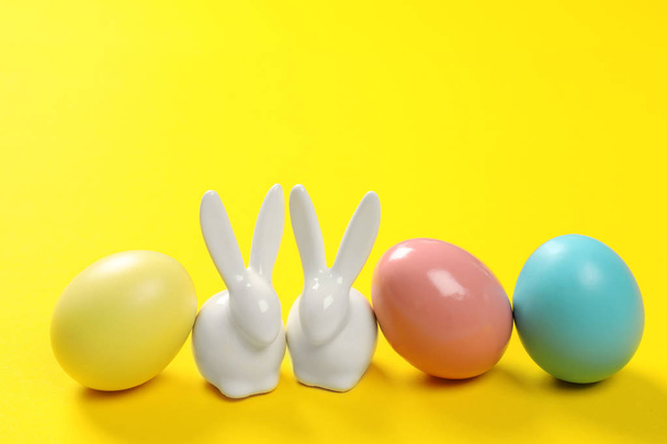Ceramic Easter bunnies and dyed eggs on color background - Foto, Imagen
