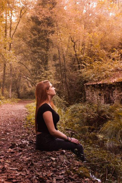 自然を見て川の近くに座っている金髪の若い女性 - 写真・画像