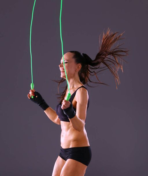 Muscular young woman standing on gray background. Muscular young woman. beautiful girl jumping rope - Φωτογραφία, εικόνα