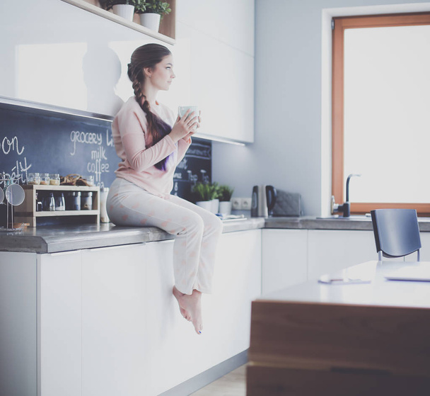 Young woman sitting on table in the kitchen. - Φωτογραφία, εικόνα