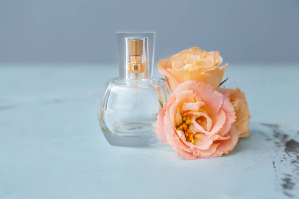 Διαφανές μπουκάλι άρωμα με όμορφα λουλούδια στο φως τραπέζι - Φωτογραφία, εικόνα