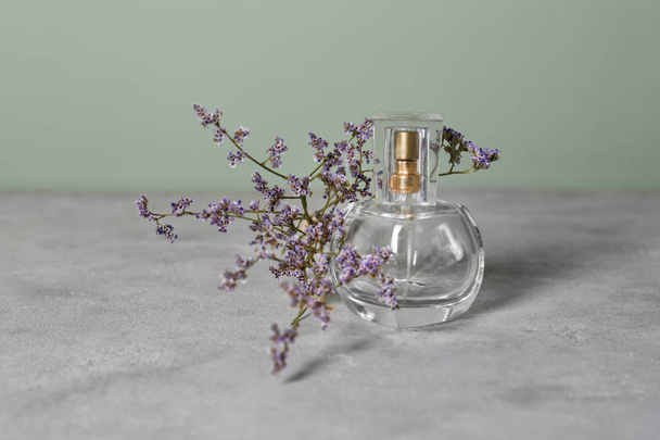 Läpinäkyvä pullo hajuvettä kauniita kukkia harmaa pöytä
 - Valokuva, kuva