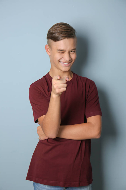 Emotional teenage boy pointing at viewer on color background - Foto, Imagem