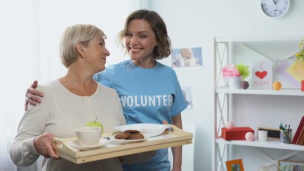 Social worker hugging retired woman holding tray with food, volunteering visit - Materiał filmowy, wideo