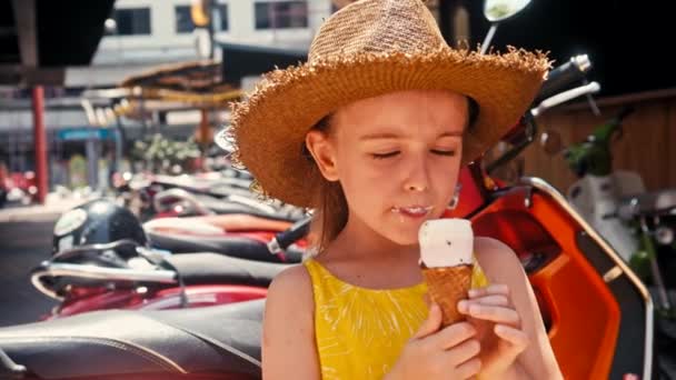 Dziewczynka w słomkowym kapeluszu jedzenia lodów na zewnątrz Street. Portret lato - Materiał filmowy, wideo
