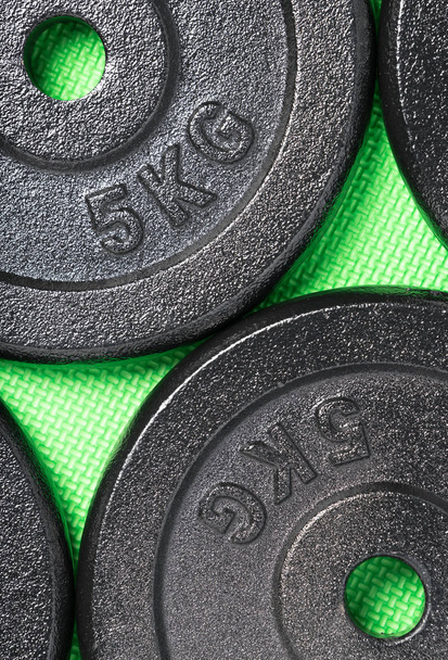 Weight plates on a colorful green floor inside a weight training gym - Photo, Image