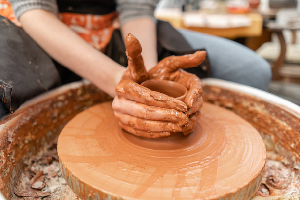 Artesano manos haciendo tazón de cerámica. Una mujer trabajando en una rueda de alfarero. Tienda familiar esculpe maceta de arcilla vista superior
. - Foto, Imagen