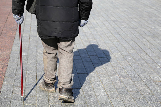 Man with walking cane on the street, rear view. Concept of limping or blind person, disability, old age, diseases of the spine - Foto, afbeelding