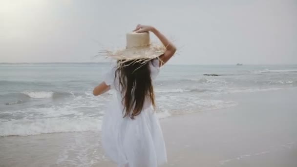 Piękne 5-7 rok stary dziewczyna z latające włosy i duży kapelusz słomkowy, biegnącej wzdłuż kinowej tropikalne ocean egzotycznych plaży - Materiał filmowy, wideo