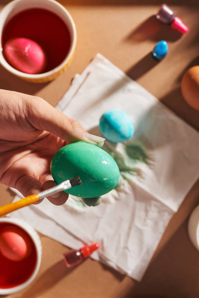 Διακοπές, παράδοση και άνθρωποι έννοια - εσωτερικη άνθρωπος χέρια Χρωματισμός αυγά του Πάσχα με βούρτσα - Φωτογραφία, εικόνα