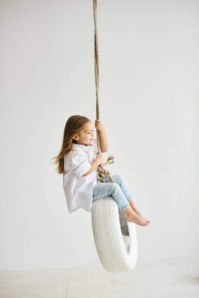 A beautiful little girl playing with a swing boat in the white r - Photo, image
