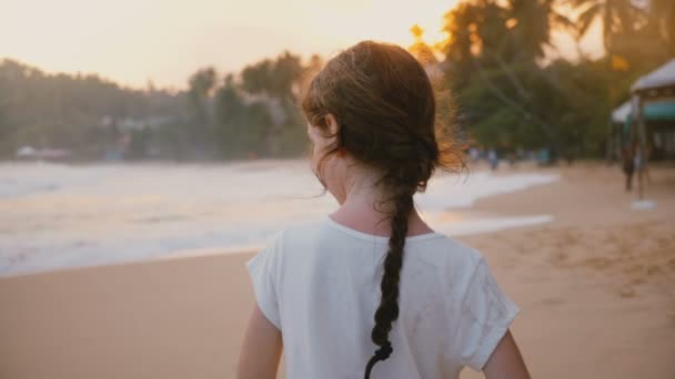 Incredibile colpo di vista posteriore di felice tranquillo piccolo 6-8 anni femmina bambino in piedi sulla soleggiata spiaggia tropicale tramonto mare
. - Filmati, video