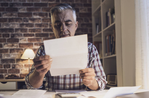 Huolestunut mies tarkistaa kotimaiset laskunsa kotona
 - Valokuva, kuva