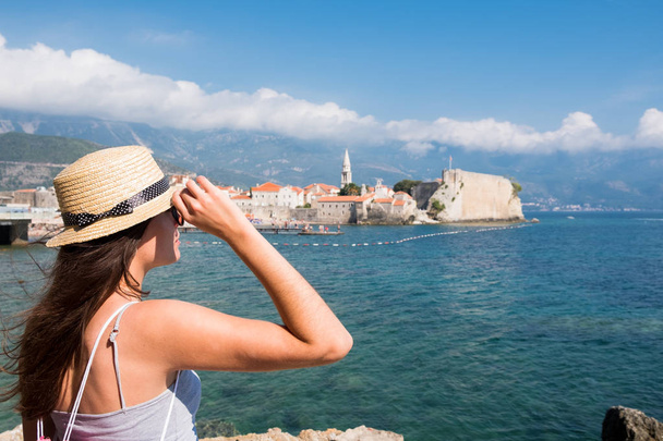 Back view of a young beautiful woman in a hat looking to the old town Budva, Montenegro - Foto, immagini