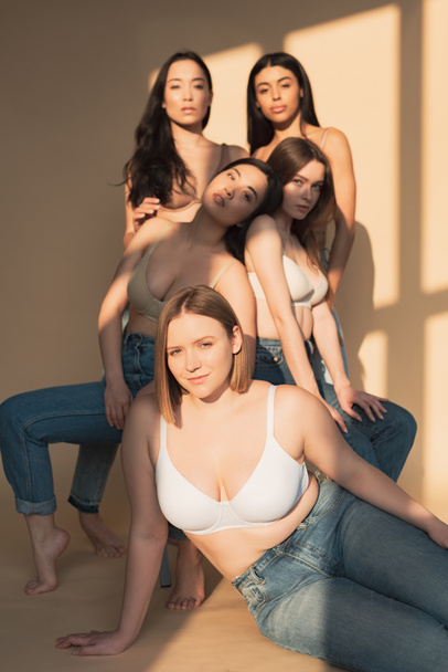 selektiver Fokus von fünf multikulturellen Mädchen, die im Sonnenlicht vor der Kamera posieren, Body-Positivity-Konzept - Foto, Bild
