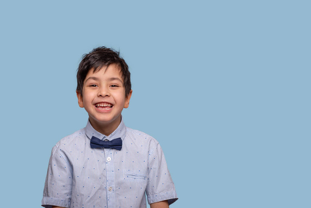 Studioaufnahme eines lachenden Jungen in blauem T-Shirt mit Schleife - Foto, Bild