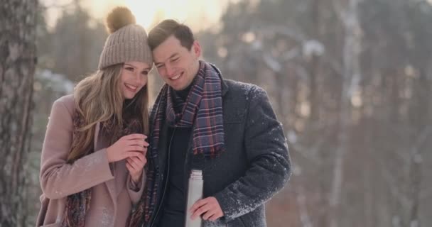 In de winter-forest naar thee drinken uit een thermos verliefde paar. Stijlvolle man en vrouw in een jas in het Park in de winter voor een wandeling. - Video