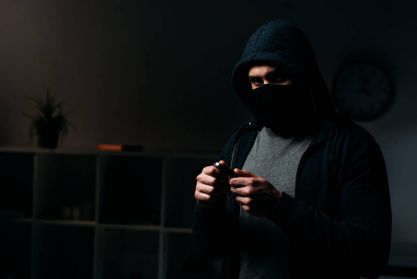 Einbrecher mit Maske steht im dunklen Raum und hält Schlüssel in der Hand - Foto, Bild