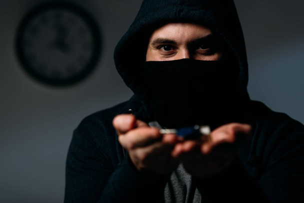 Verbrecher in Kapuzenpulli und Maske zeigt Schlüssel vor Kamera - Foto, Bild