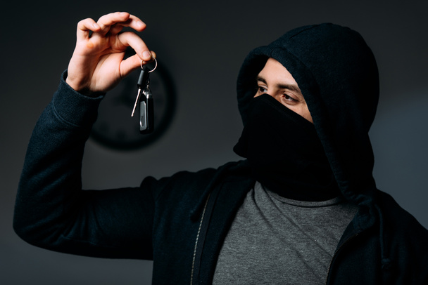 Criminal in black mask and hoodie looking at keys - Photo, Image