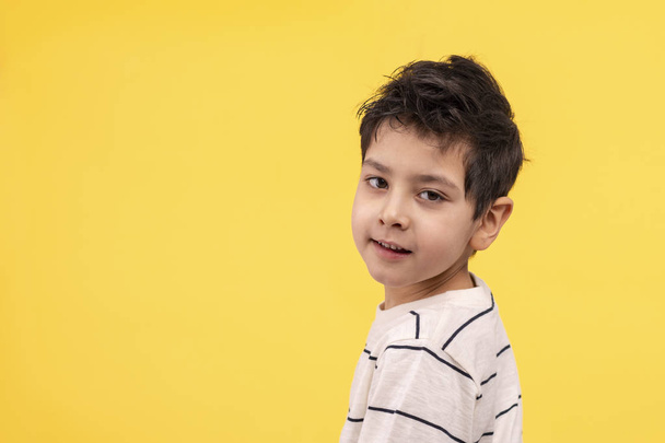 Студийный снимок улыбающегося мальчика в белой футболке на жёлтой спине
 - Фото, изображение