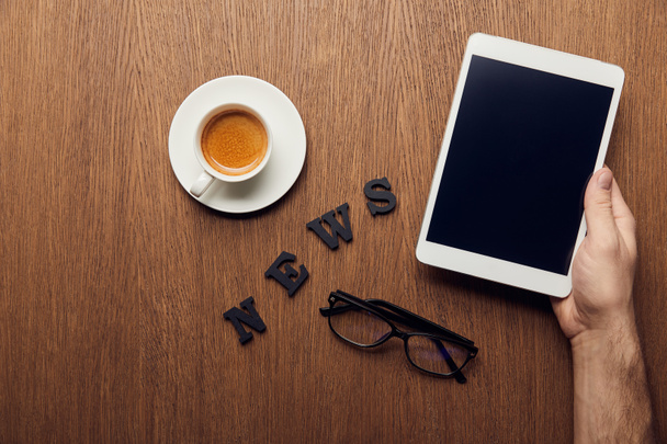 обрезанный вид человека, держащего цифровой планшет с чистым экраном возле букв новостей, чашки кофе и стаканов
 - Фото, изображение