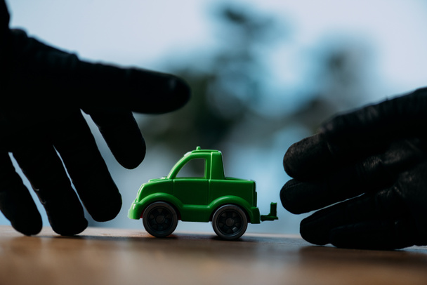 Partial view of thief in black gloves stealing toy car - Photo, Image