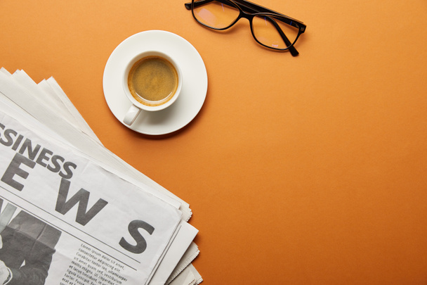 pohled shora brýlí u obchodní noviny a šálek kávy na oranžové  - Fotografie, Obrázek