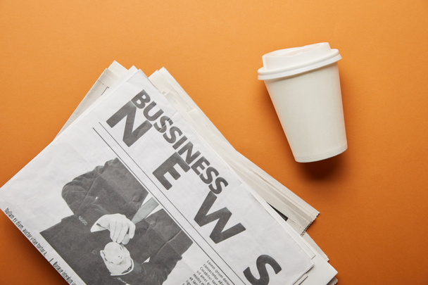 top view of business newspaper near paper cup with drink on orange  - Foto, afbeelding