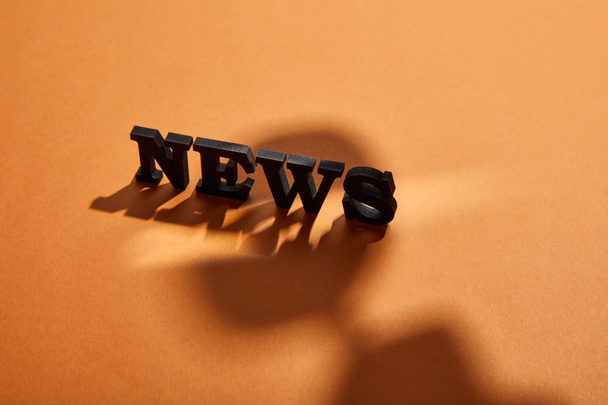 black news lettering with copy space near shadows on orange  - Photo, image