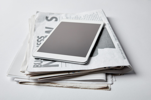 tablet digital com tela em branco perto de jornais de negócios com artigos sobre branco
  - Foto, Imagem