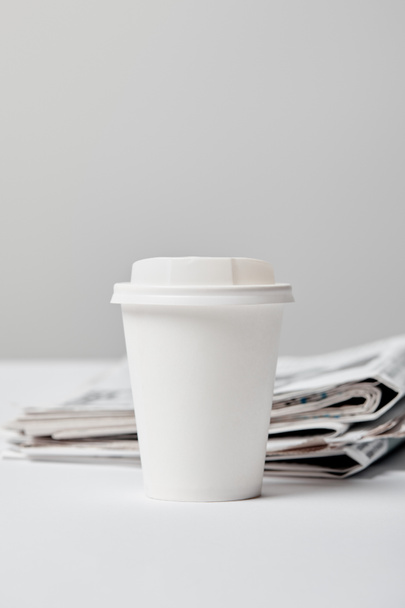 selectieve aandacht van papier cup in de buurt van kranten op grijs  - Foto, afbeelding