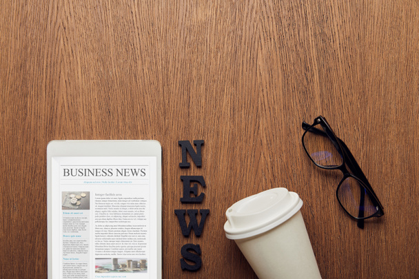 vista superior de la tableta digital con noticias de negocios en la pantalla cerca de las letras de noticias, gafas y taza de papel
  - Foto, imagen