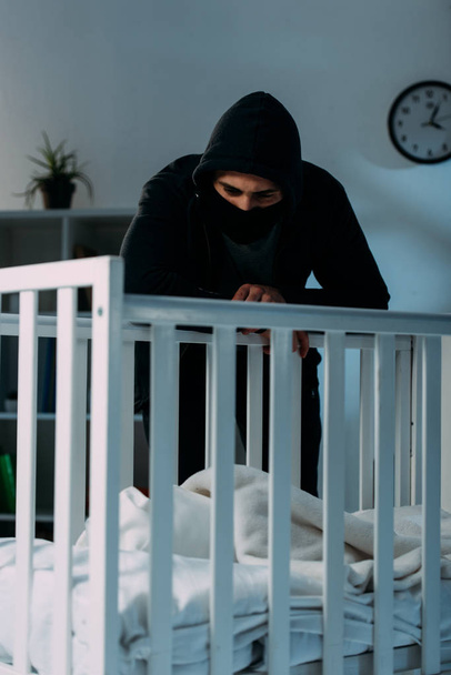 Pensive kidnapper standing in dark room and looking in crib - Foto, imagen