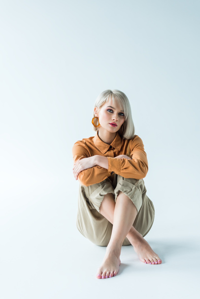 beautiful stylish young woman sitting with crossed legs and looking at camera on white - Фото, зображення