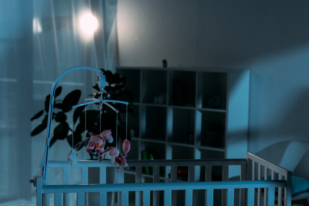 Crib ja vaaleanpunainen mobiili lelujen kanssa pimeässä lastentarhassa
 - Valokuva, kuva