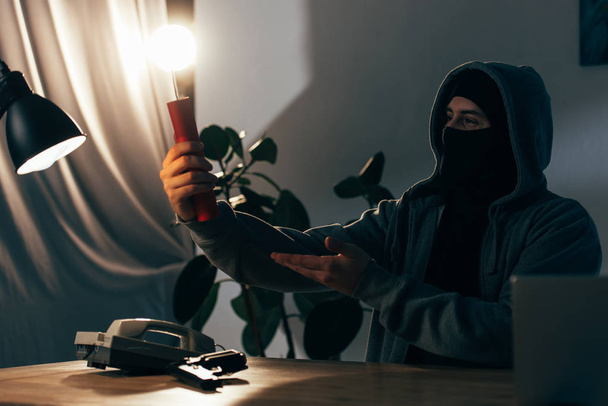 Pleased terrorist in mask holding lighted dynamite in room - Photo, Image