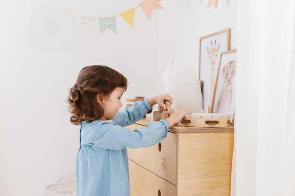 Little girl wearing light blue dress playing in children room scandinavian style. - Фото, зображення