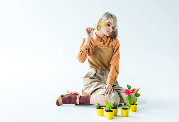 mooie stijlvolle meisje zittend en poseren met fern blad en bloem potten op wit - Foto, afbeelding