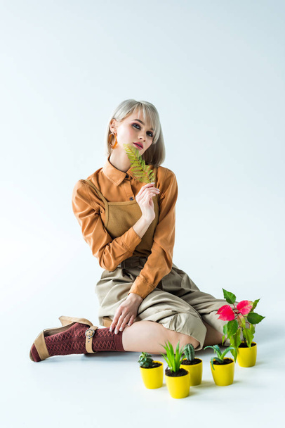 beautiful stylish girl posing with fern leaf near flower pots on white - Zdjęcie, obraz